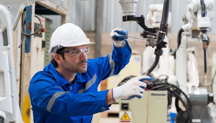 Male engineer worker using screwdriver maintenance automatic welding robotic arm machine in factory. Male technician worker checking, repair automatic welding robot arm machine at production line