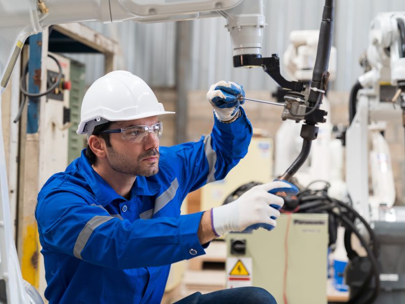Male engineer worker using screwdriver maintenance automatic welding robotic arm machine in factory. Male technician worker checking, repair automatic welding robot arm machine at production line