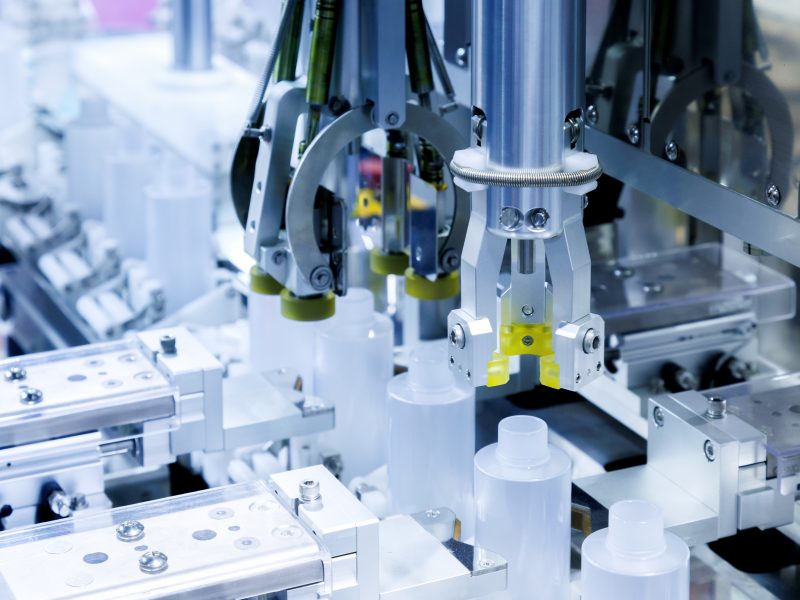 robot arm moving plastic bottle to conveyor belt of auto capping and labeling machine at cosmetic and skin care manufacturing. cosmetic industry and ai technology machinery concept.